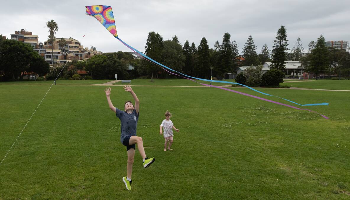 Flynn and Marley Burgess chase a kite near Nobbys foreshore. Picture by Jonathan Carroll