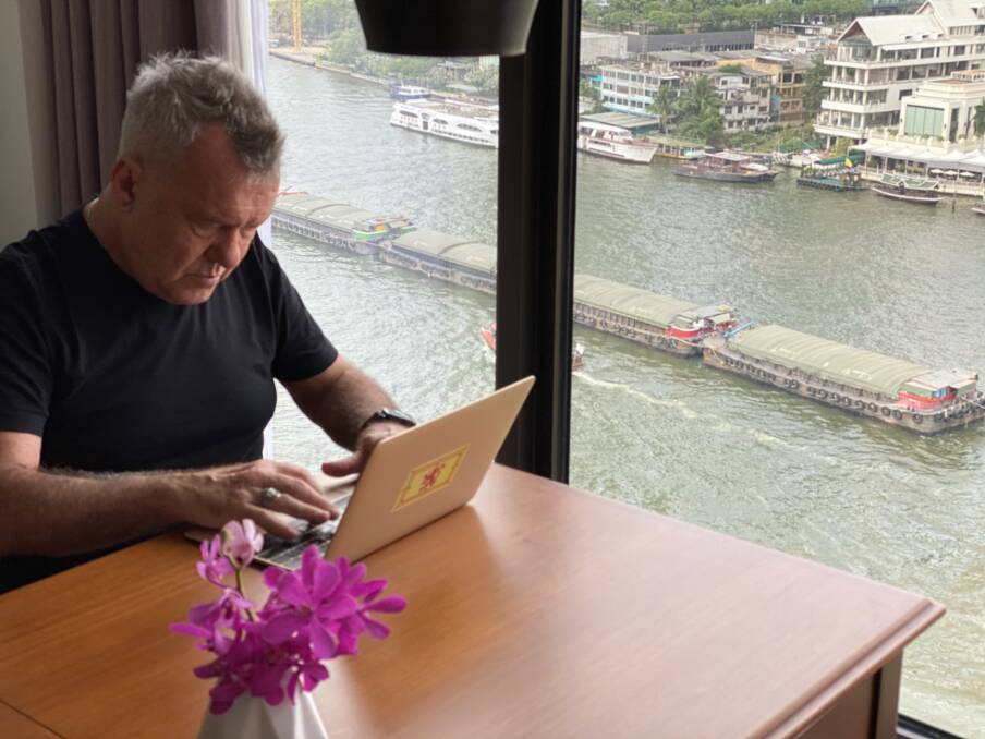 On the road: Jimmy writing in Thailand, as rice barges on the Chao Phraya pass by.
