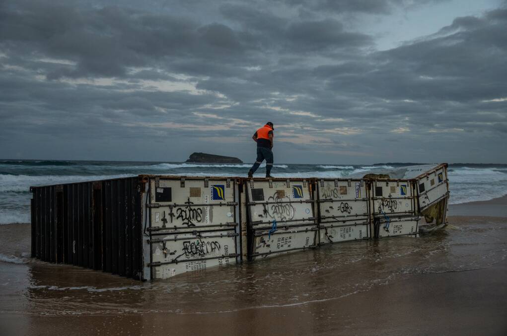 Running A Tight Ship: A man runs across shipping containers washed up on Birdie beach on the Central Coast. Picture: Marina Neil 