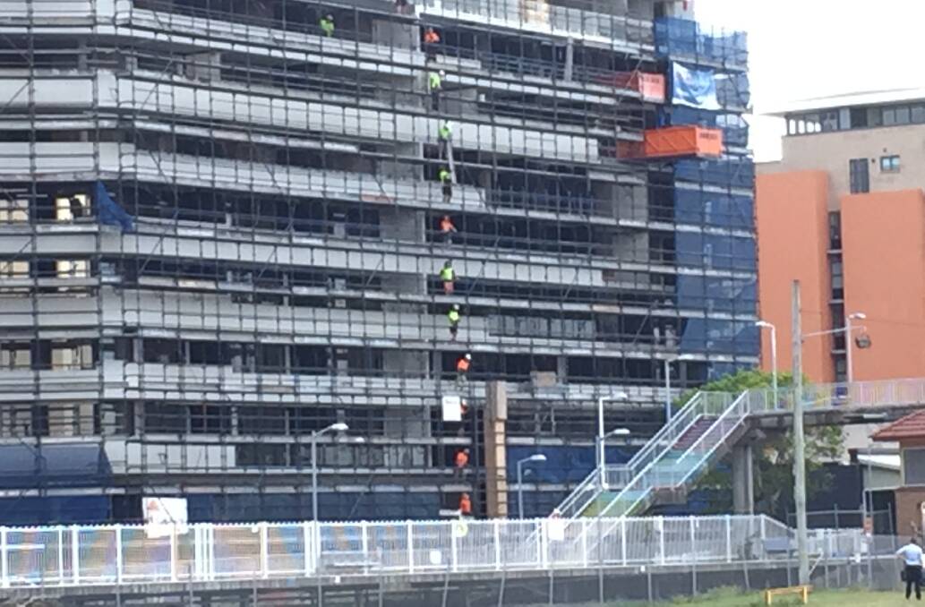 Workers in fluoro in a line on a building near Honeysuckle.  
