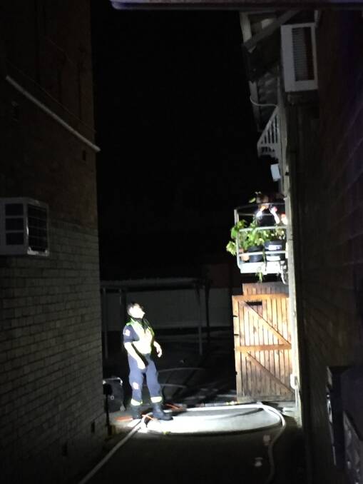 A fire brigade officer talks to a colleague on the balcony of the unit where the fire broke out on the first floor of the shopping strip in Belford Street, Broadmeadow, on Sunday evening. Picture: Ian Kirkwood