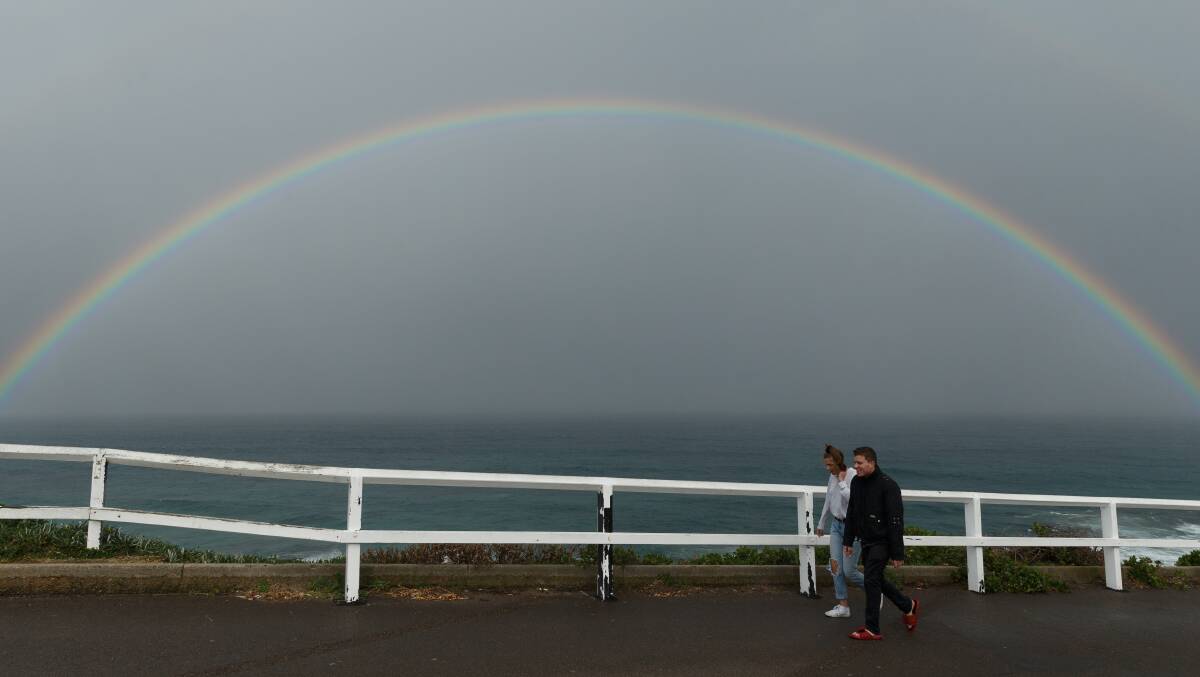 FORECAST: Walkers brave the rain on the Bathers Way at Bar Beach as a very close rainbow shines over the ocean. Picture: Max Mason-Hubers 