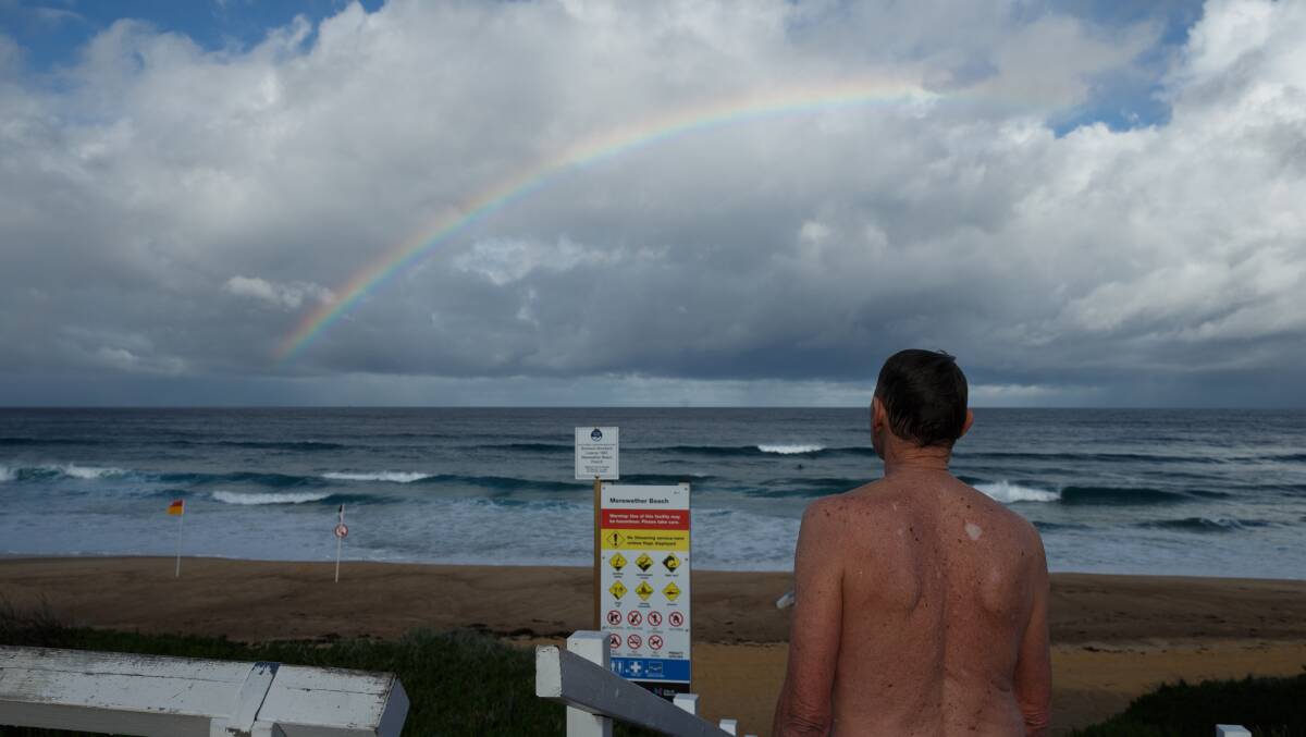 RAINS ARE COMING: Michael Smith looks out at a rainbow shining over the ocean at Merewether beach after having a swim during one of a series of rain squalls. Picture: Max Mason-Hubers