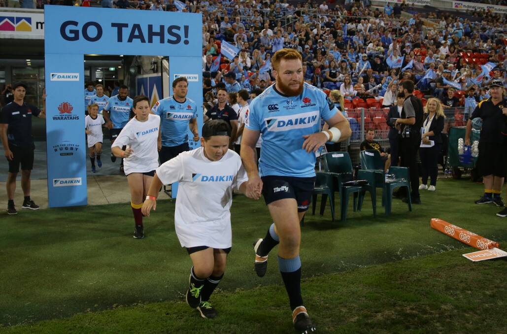 GO TAHS: Harry Johnson-Holmes and a local junior run out onto the field at McDonald Jones Stadium. Picture: Jonathan Carroll
