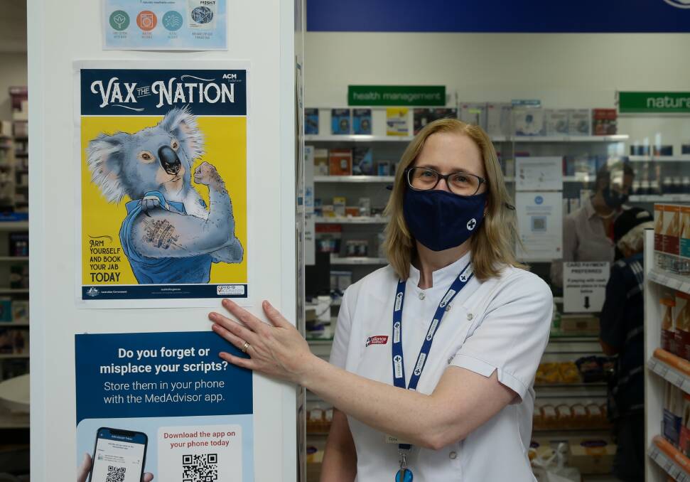 ROLL UP YOUR SLEEVES: Merewether Pharmacy owner Fiona Evans putting up ACM's Vax the Nation campaign poster. Picture: Jonathan Carroll