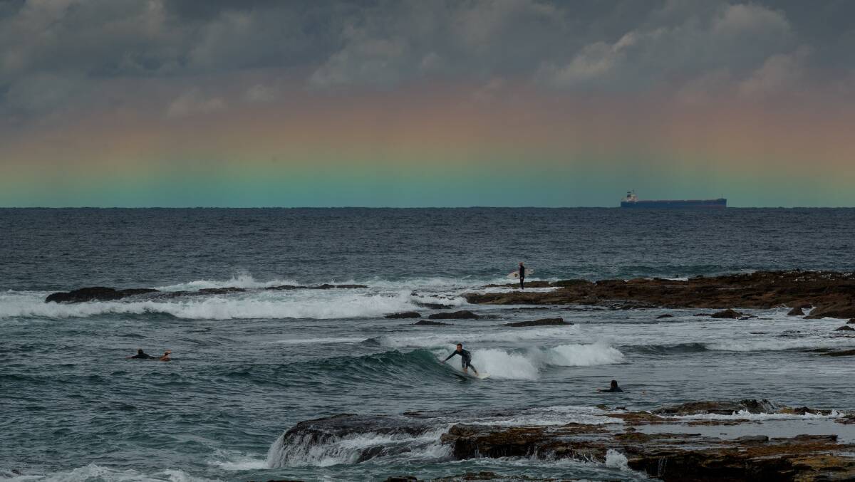 HORIZON: A large flat rainbow shines over the ocean behind a surfer at the Cowrie Hole on Wednesday, ahead of big swell predicted from tonight. Picture Max Mason-Hubers