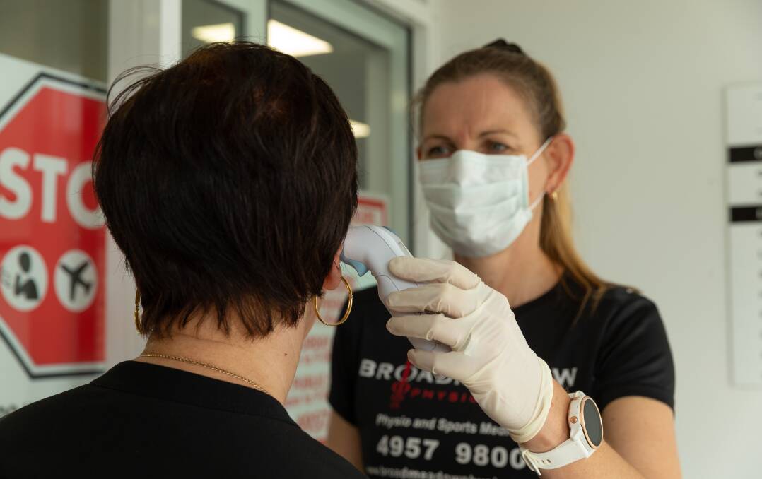 Cheryl Gillard demonstrates with a thermometer on Anna Fable how Broadmeadow Medical Centre centre has begun checking the temperature of everyone before allowing them in the building. Picture: Max Mason-Hubers