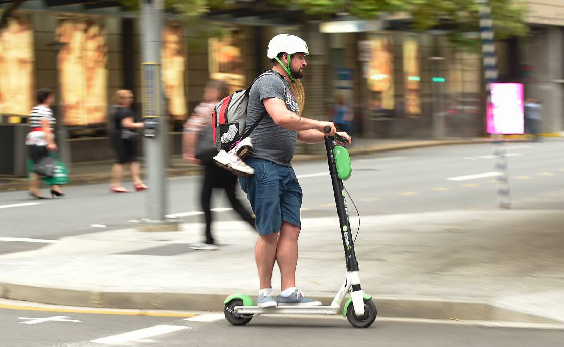 A man crosses a street on a Lime e-scooter in Brisbane's central business district in December. 