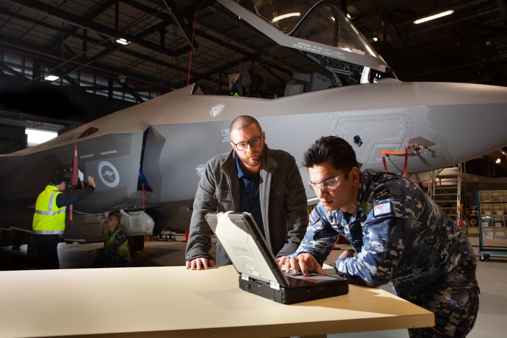 (L-R) Aaron Piccinin from CIOG works with Leading Aircraftman Kevin McDonald, an Aircraft Structural Technician (ASTTECH) with No. 3 Squadron on the wirelessly connected Portable Maintenance Aid laptop during routine maintenance of an F-35A Lightning II at RAAF Base Williamtown. Picture: Christopher Dickson