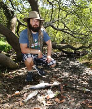Looking for answers: Tighes Hill resident Jonathon Love with some of the dead fish. Picture: Peter Lorimer