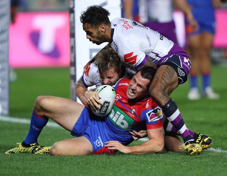 Man-handled: Knights skipper Mitchell Pearce is sandwiched in a tackle after being trapped in his own in-goal as the Melbourne Storm poured on the pressure in the first half on Saturday night. Picture: NRL Photos.