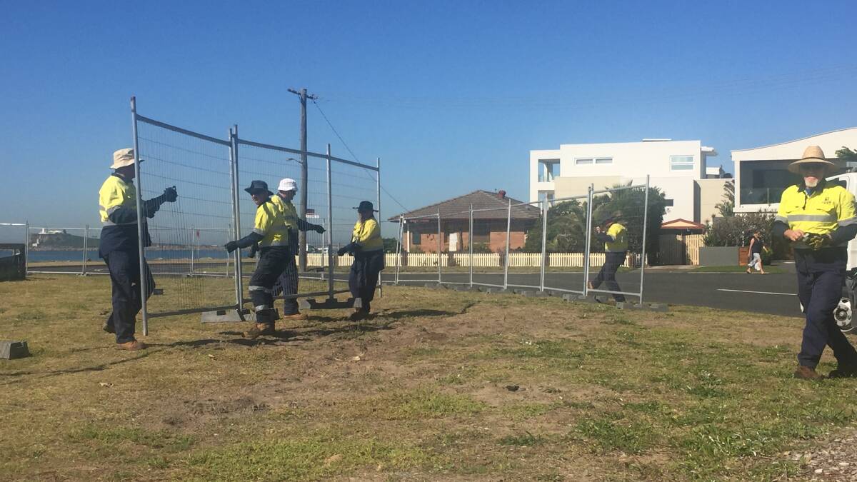 UNDER THREAT: City of Newcastle workers move an erosion exclusion fence to within a metre of a main road at Stockton on Wednesday morning. 