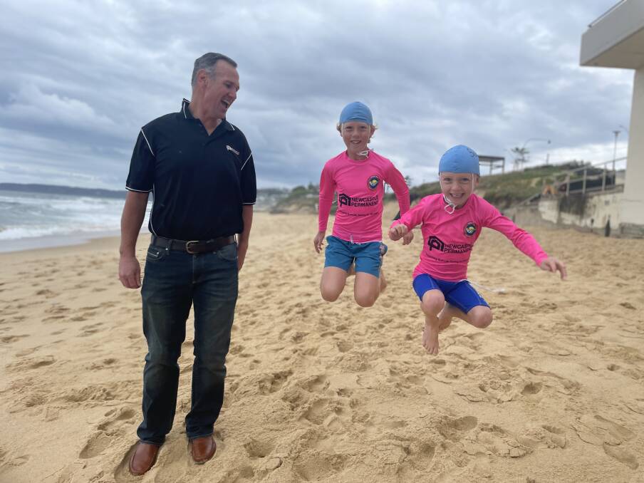 Newcastle Permanent chief financial officer Mark Colless, which supports the program, with Nippers Theo and Sully Moulton at Bar Beach. Picture supplied.