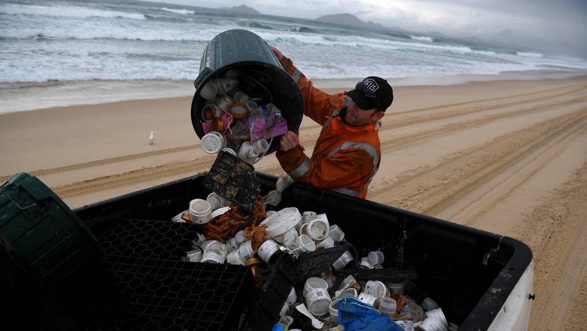 CLEAN UP: A worked collects rubbish from a Port Stephens beach. Picture: AAP/Dan Himbrechts