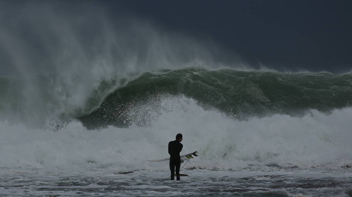 BRAVE: A surfer heading out into huge seas at Merewether beach on Saturday. Pictures: Simone De Peak