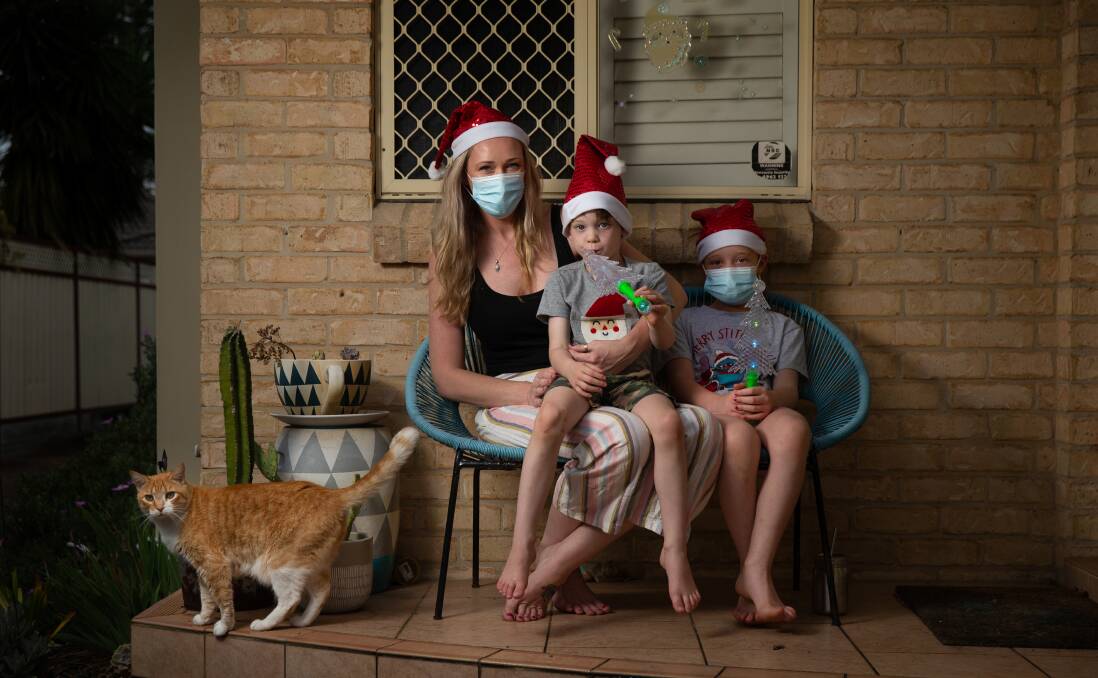 MAKING THE MOST OF IT: Charmaine Sorrenson, 33, and her two children Eli, five, and Emma, seven - who all have COVID-19 - and the family's cat, Oompa, outside their Adamstown home on Thursday. Picture: Marina Neil