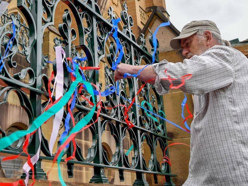 Paul Auchettl ties ribbons in support of other abuse survivors to the fence of St Mary's Cathedral. (Bianca De Marchi/AAP PHOTOS)
