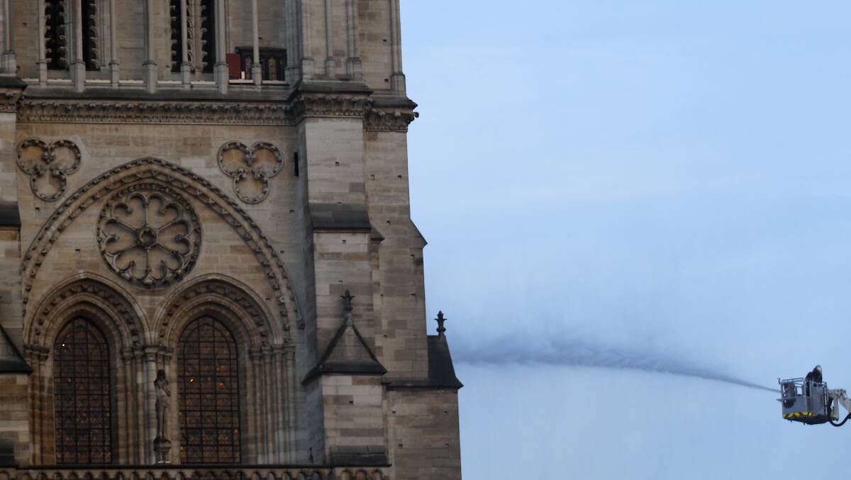 A fire fighter tackles the blaze as flames and smoke rise while Notre Dame cathedral is burning in Paris, Monday, April 15, 2019. A catastrophic fire engulfed the upper reaches of Paris' soaring Notre Dame Cathedral as it was undergoing renovations Monday, threatening one of the greatest architectural treasures of the Western world as tourists and Parisians looked on aghast from the streets below. (AP Photo/Francois Mori)