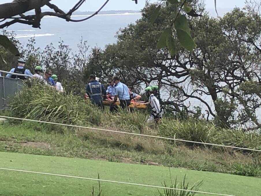 Fall: Police and ambulance officers carry a man from a cliff at Crackneck Lookout, Bateau Bay shortly before 1pm after he was rescued following a hang-gliding incident. 