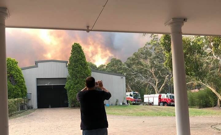 Close: Charmhaven real estate agent Darin Butcher at his home on New Year's Eve as fire rears up in bush behind his property. Police believe the fire that caused the evacuation of hundreds of people was deliberately lit. 