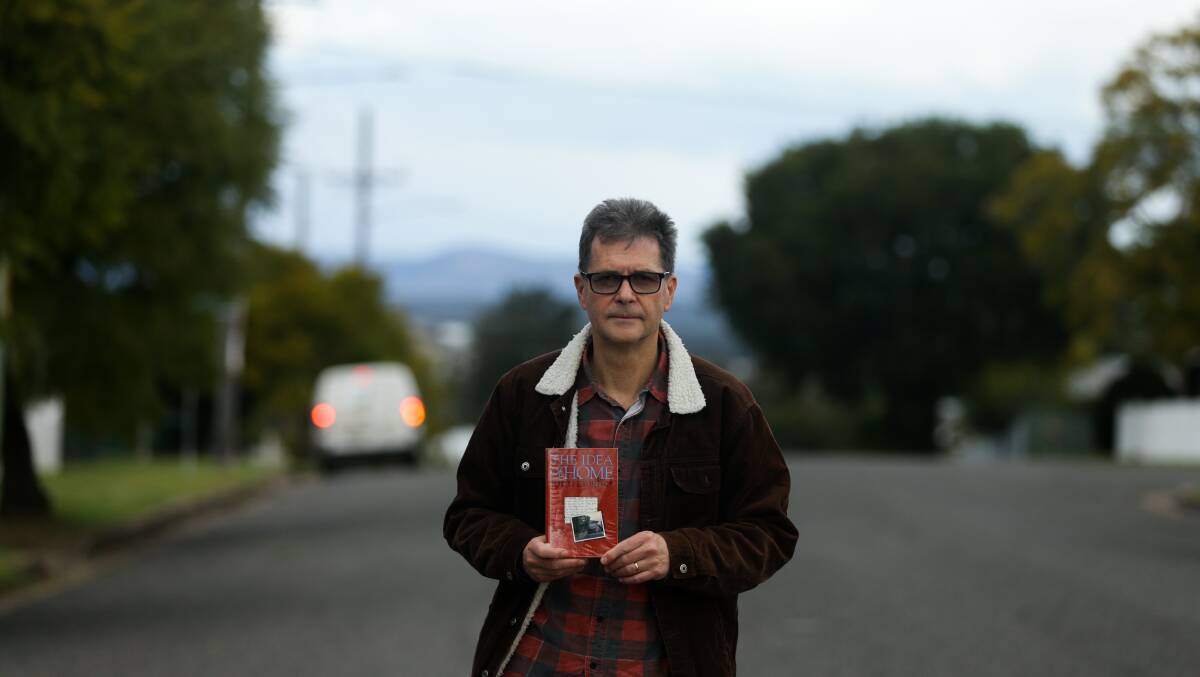 John Hughes in the Cessnock street where he grew up, holding a copy of 'The Idea of Home'. Picture: Jonathan Carroll