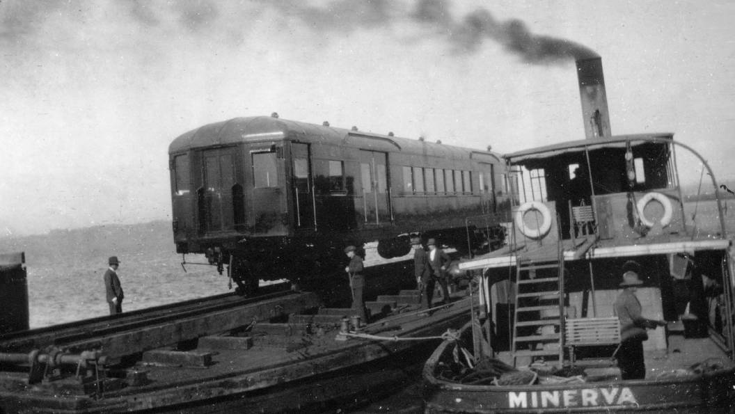 A new electric rail carriage is carried across the harbour from Walsh Island on a barge propelled by steam tug, the "Minerva". Picture: ARHS/NSW Rail Resource Centre
