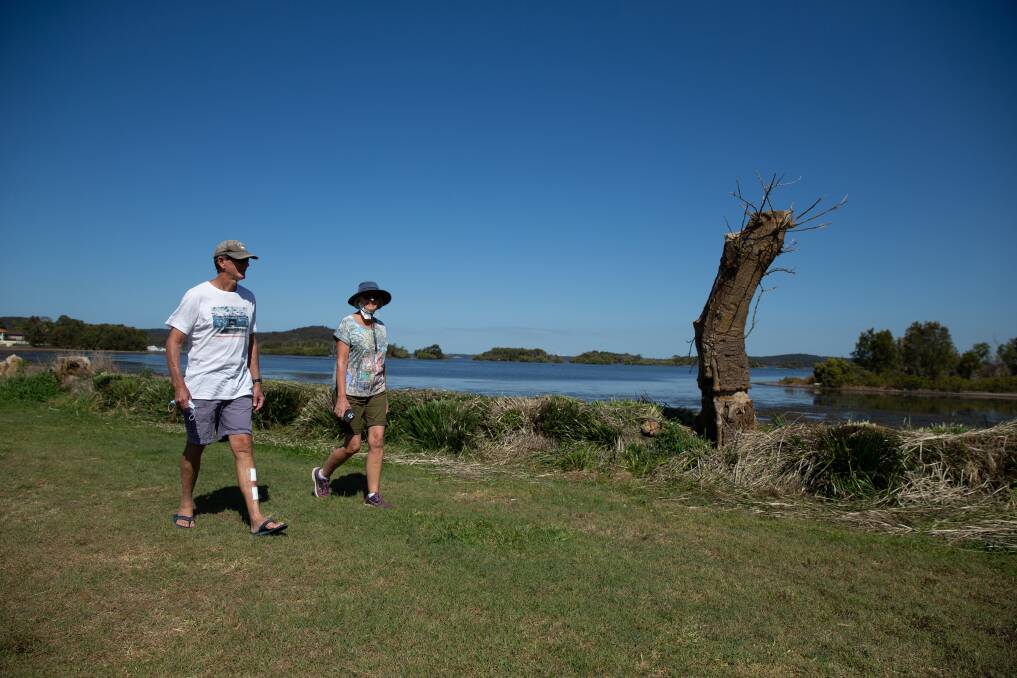 Swansea residents Suzanne and Brian Chivers pass the cut lomandra along the shore. Picture: Marina Neil