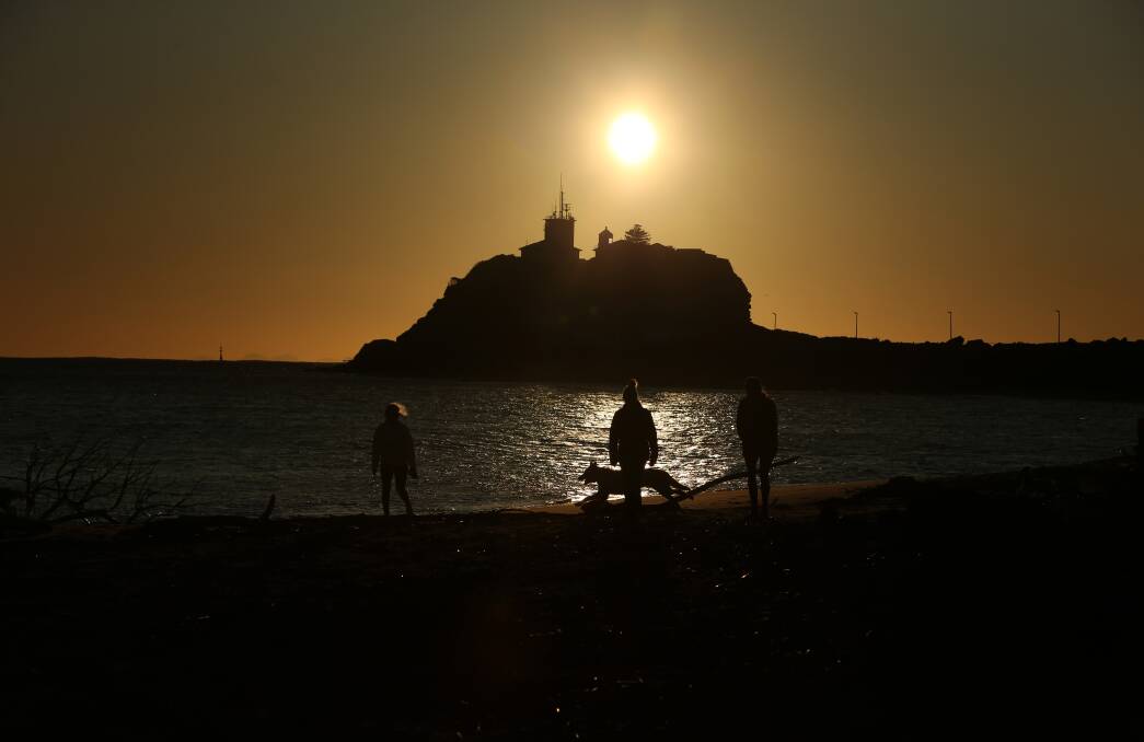 Early morning walkers on the 'Dog Beach', as the sun rises over Nobbys. Picture by Simone De Peak 
