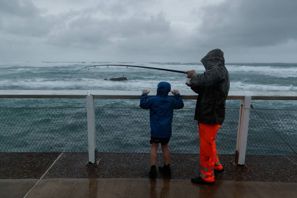 WET: Phil and Jett Lowas fishing on the bathers way at Nobbys Beach on Sunday. 