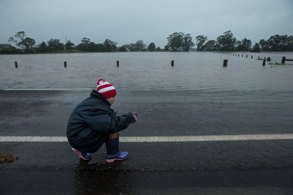BIG WET: Nicholas Tobin, 11, at Osterley, near Nelsons Plains, on Sunday crouches on the road near a paddock completely underwater. Picture: Marina Neil 