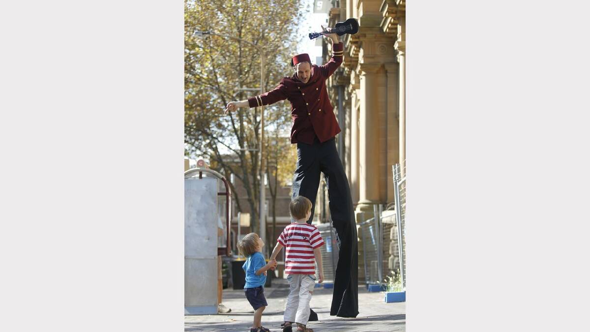 Stilt performer Ross Brown in front of  the old Newcastle post office, watched by Aiden, 2 and Owain, 6 from Lambton. Picture Natalie Grono