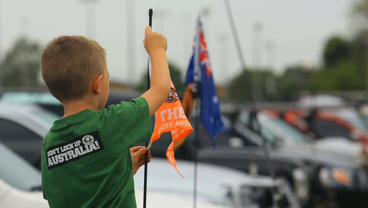 A young boy attaches a protest flag to the aerial of the family 4WD at the Unlock Australia Rally in Newcastle this month.  Picture: Peter Stoop