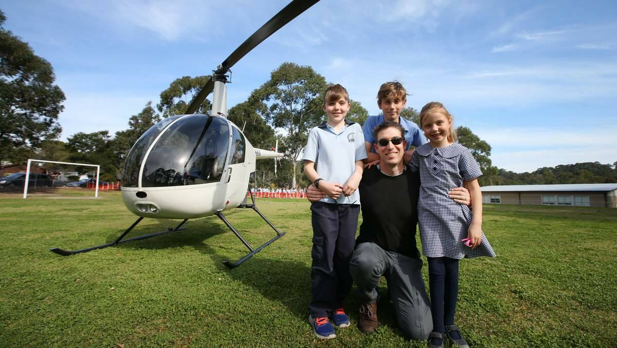 Dwayne Sharrock, a helicopter pilot, with his children Riley, Ethan and Jenna at Eleebana Public School, Mr Sharrock flew the helicopter to school as part of a presentation on careers - and machines, large and small. Picture Dean Osland.