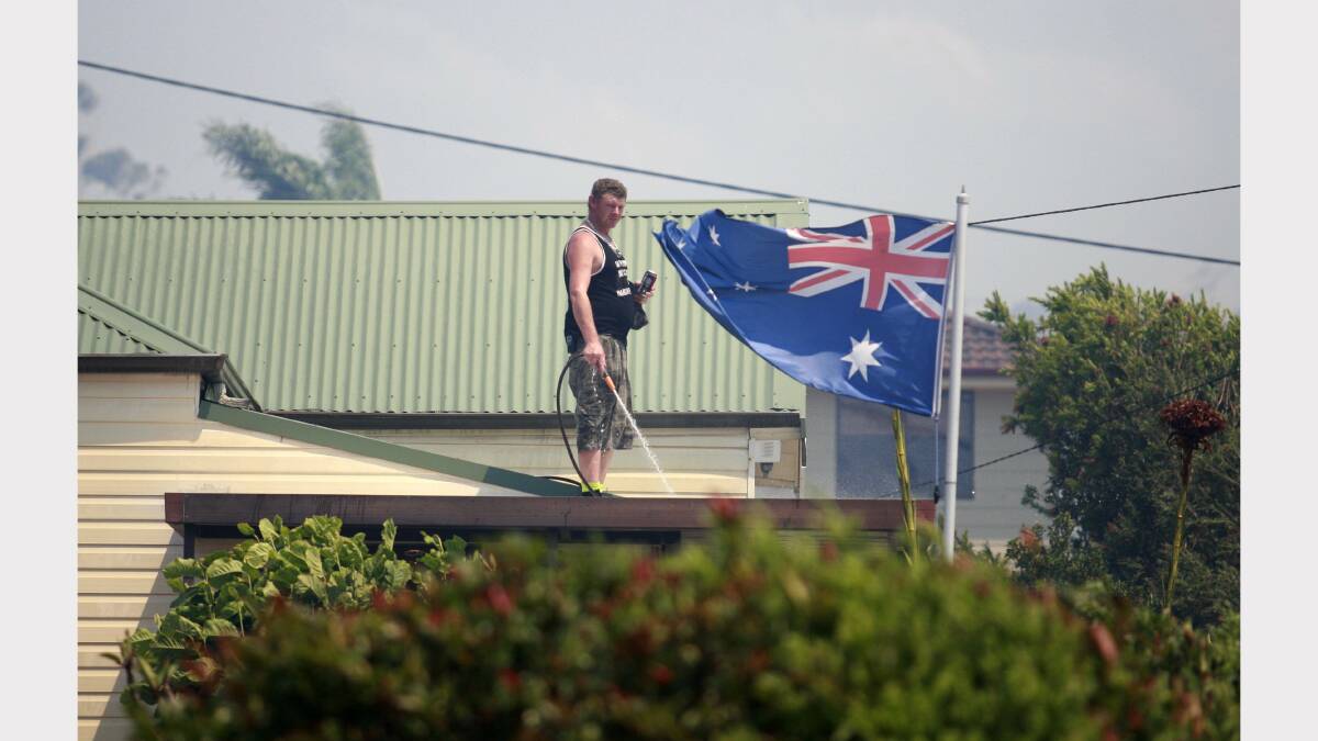 Minmi resident Troy Mills of  Woodford Street on his roof hosing down in preparation for the fire. Picture by Peter Stoop.
